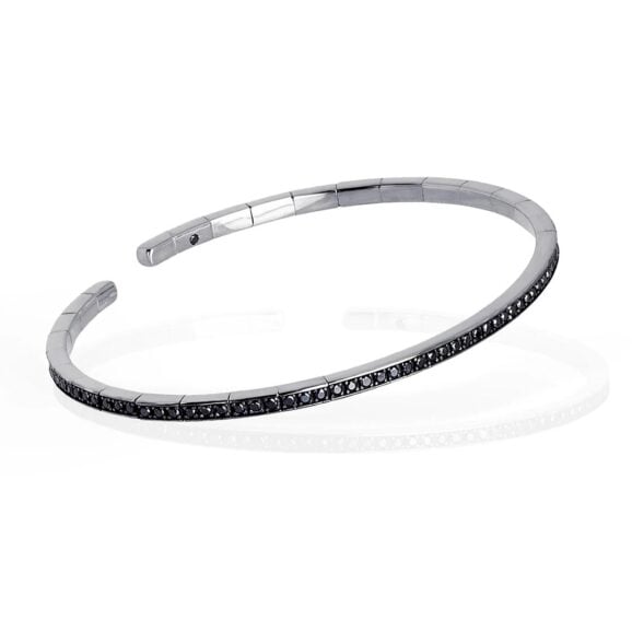 elastična, polu kruta narukvica od 18 kt belog zlata ukrašena sa ukupno 99 Crnih Dijamanata. Elastična narukvica je karakterisana dugim nizom od 99 crnih dijamanata ukupne težine od 0,99 karata koji prekrivaju deo cele narukvice. Unutar narukvice, kao garancija brenda MANO|J., postavljen je crni dijamant od 0,01 ct. Ova prefinjena, elegantna i savršeno nosiva narukvica odiše luksuzom. Ova narukvica se pravi u nekoliko veličina i odgovara i muškarcima i ženama. Istraži manje ženske narukvice ili šire muške narukvice sa Crnim Dijamantima, utkanim u 18 kt belo zlato.