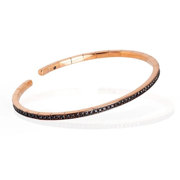 elastična, polu kruta narukvica od 18 kt roze zlata ukrašena sa ukupno 99 Crnih Dijamanata. Elastična narukvica je karakterisana dugim nizom od 99 crnih dijamanata ukupne težine od 0,99 karata koji prekrivaju deo cele narukvice. Unutar narukvice, kao garancija brenda MANO|J., postavljen je crni dijamant od 0,01 ct. Ova prefinjena, elegantna i savršeno nosiva narukvica odiše luksuzom. Ova narukvica se pravi u nekoliko veličina i odgovara i muškarcima i ženama. Istraži manje ženske narukvice ili šire muške narukvice sa Crnim Dijamantima, utkanim u roze zlato.