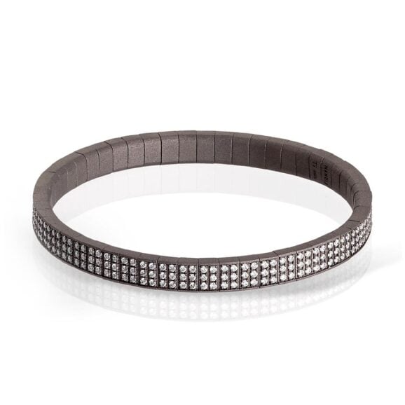 Muška narukvica od titanijuma, belog zlata 18 kt i belih dijamanata. Duga serija zglobnih elemenata od titanijuma povezanih međusobno čini elastičnu narukvicu. Na svakom elementu je ukrašeno 6 belih dijamanata, ukupne težine od 3.12 ct. Da bi se dodatno obogatila narukvica, umetnut je element od belog zlata 18 kt sa 6 belih dijamanata, ukupne težine od 6 tačaka. Dragoceni dragulj u kome su zlatarska majstorija, inovacija i poznavanje materijala brenda MANO|J. uspeli da stvore remek-delo visokih vrednosti.