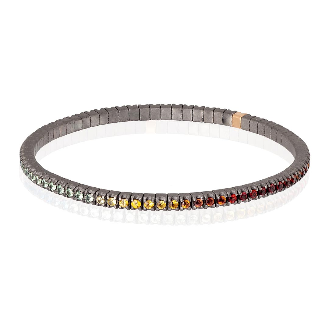 Muška narukvica od titanijuma i 18k zlata, sa rainbow safirima model tenbrtzamulrg3pt_p-5 Muška elastična tenis narukvica od titanijuma i višebojnih safira (2,69 ct). Narukvica se sastoji od neprekidnog niza kamenja težine po 0,03 tačke postavljenih na titanijumske segmente, sa jednim kamenom ufasovanim u 18 kt roze zlato. Svaki se nalazi jedan pored drugog na elastičnoj vezi. Ova narukvica spaja ideju klasičnog tenis nakita sa inovacijom materijala, čineći je laganom, sigurnom i lakom za nošenje.