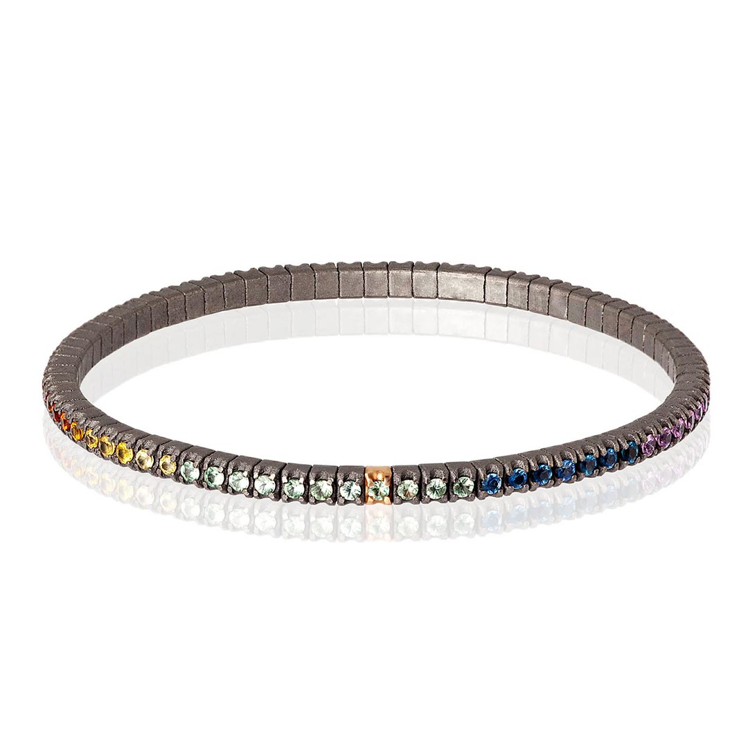 Muška narukvica od titanijuma, sa rainbow safirima model tenbrtzamulrg3pt_p Muška elastična tenis narukvica od titanijuma i višebojnih safira (2,69 ct). Narukvica se sastoji od neprekidnog niza kamenja težine po 0,03 tačke postavljenih na titanijumske segmente, sa jednim kamenom ufasovanim u 18 kt roze zlato. Svaki se nalazi jedan pored drugog na elastičnoj vezi. Ova narukvica spaja ideju klasičnog tenis nakita sa inovacijom materijala, čineći je laganom, sigurnom i lakom za nošenje.