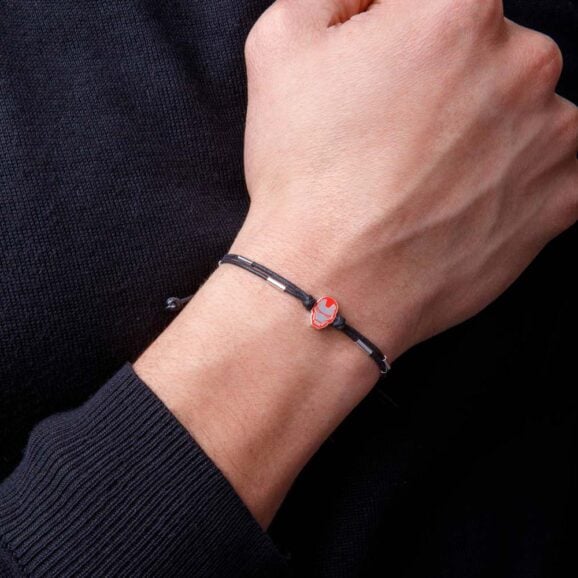 Crna narukvica od uzeta na zglobu sa malim priveskom u obliku maske iron man u crveno-zlatnoj boji, sa podesivim krajevima i čvorićima